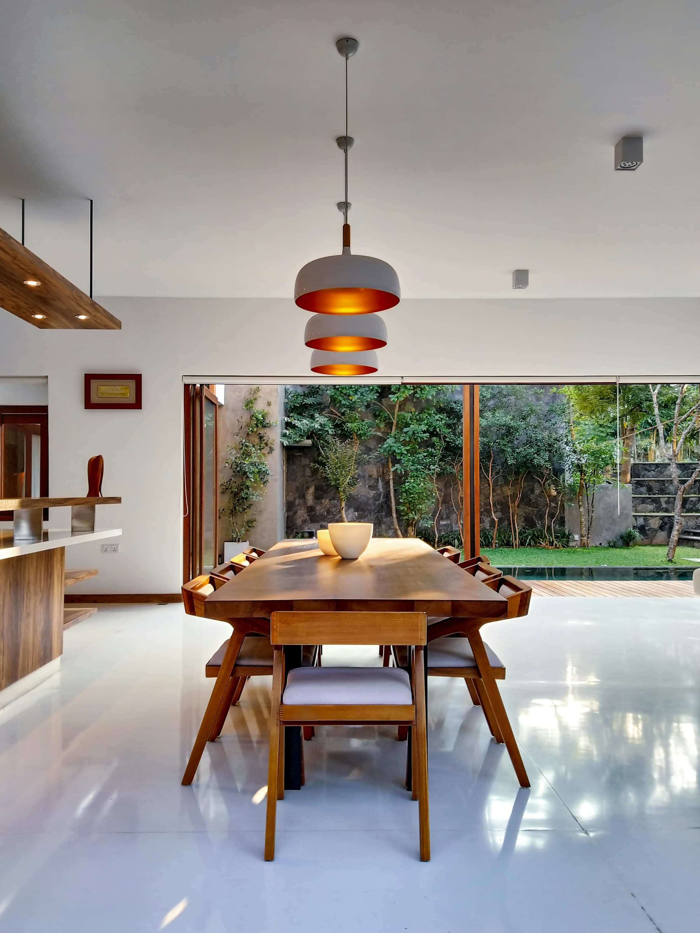 Timber dining table under pendant lights overlooking an enclosed garden.