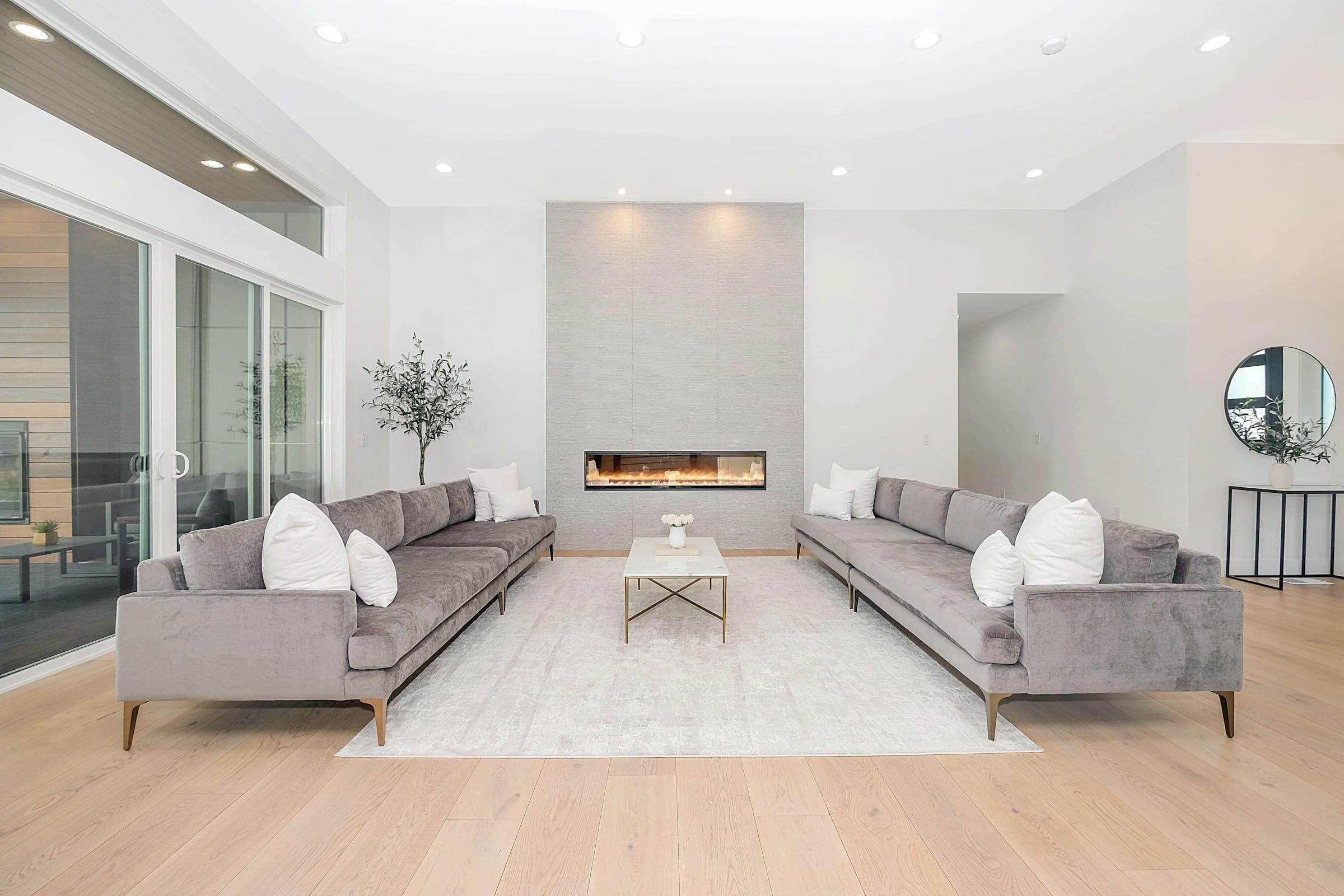 Symmetrical pale living room with two grey sofas, oak floor and linear fireplace.