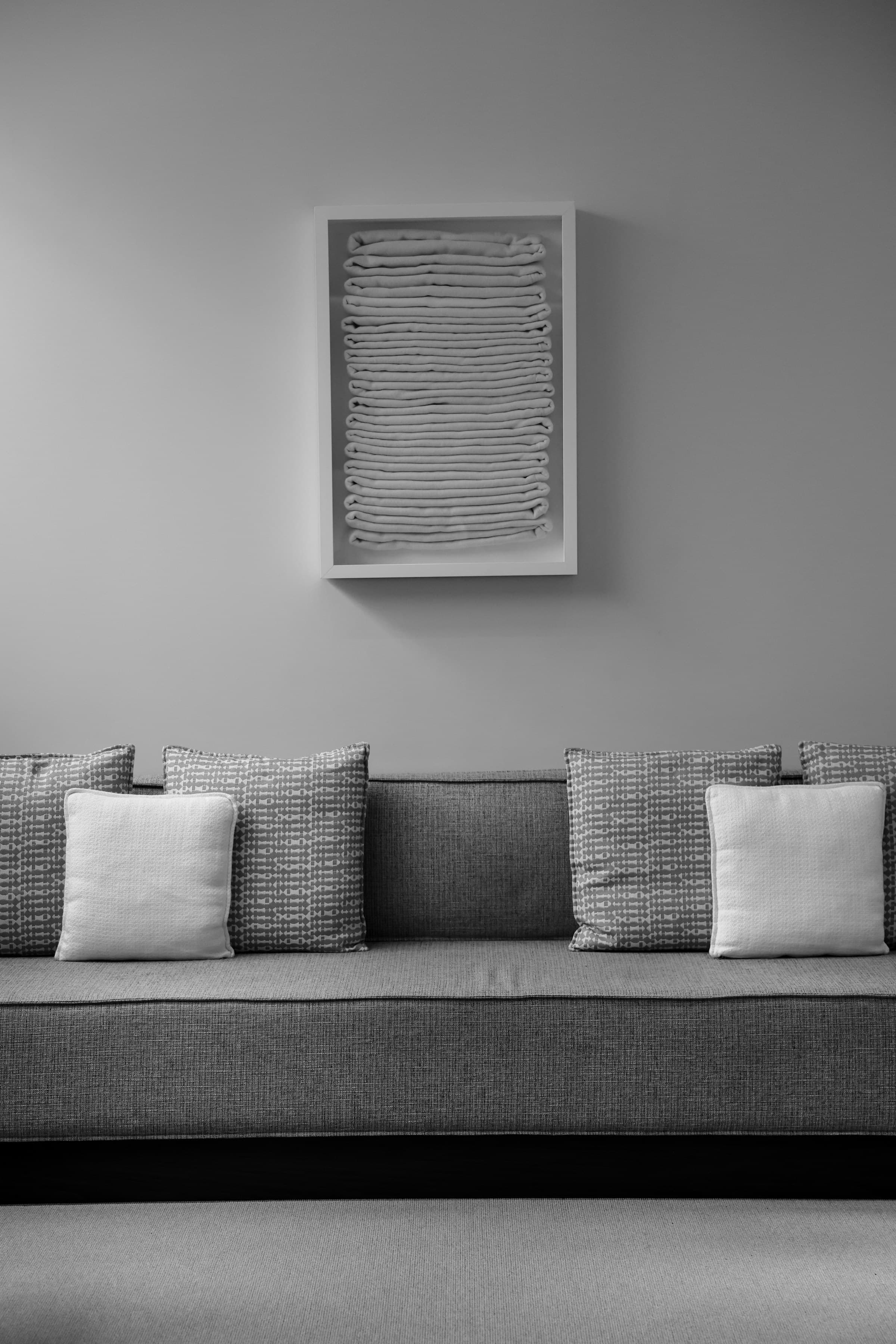 Monochrome sofa with textured cushions and a framed textile artwork.
