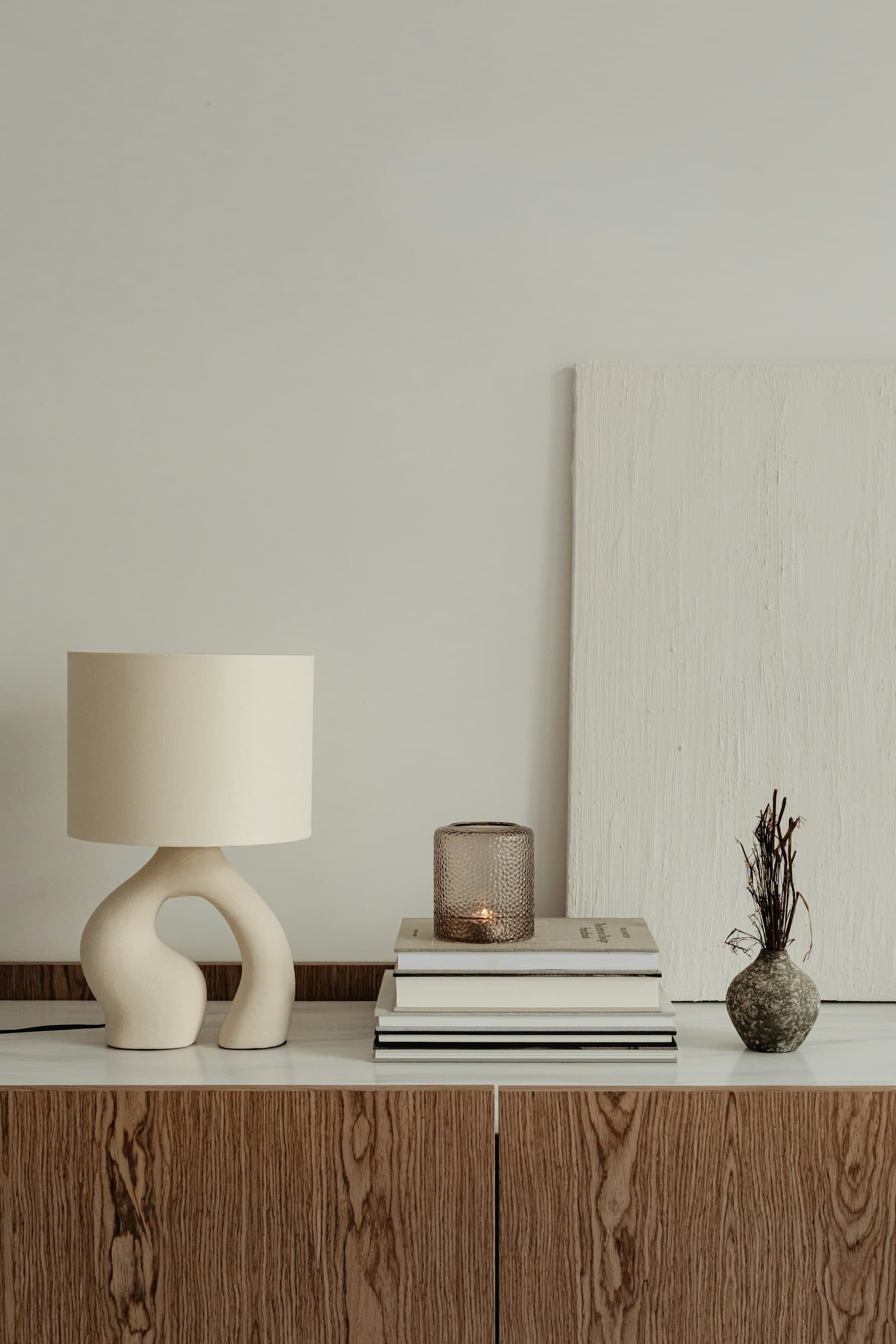 Sculptural cream lamp, books and ceramic vessels on a timber sideboard.