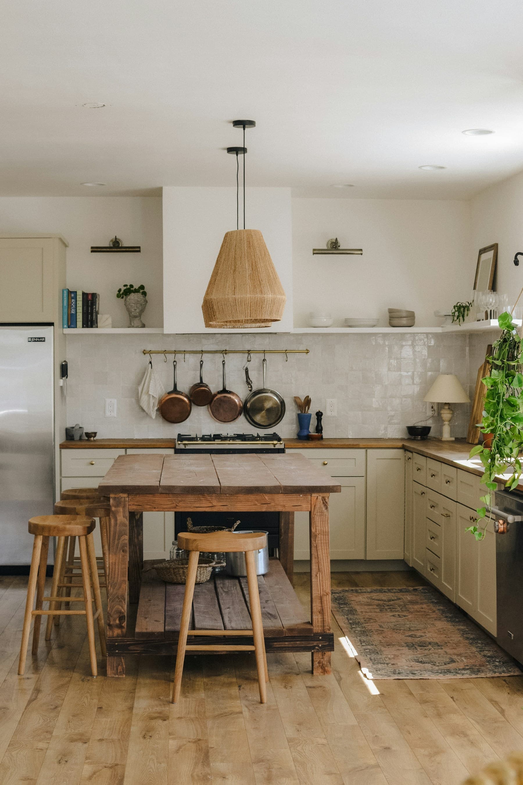 Front view of cream kitchen with timber island, stools and woven pendant.