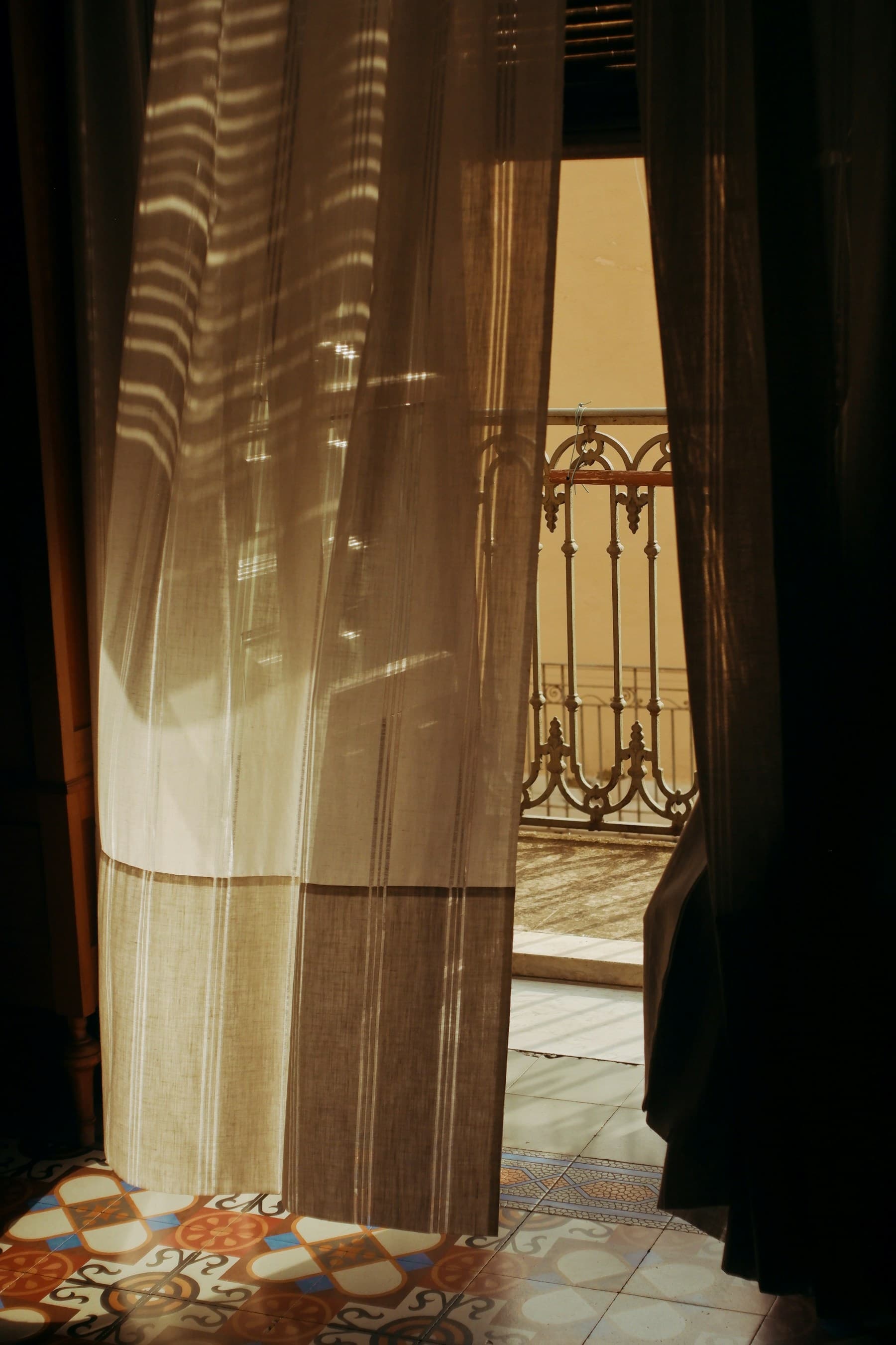 Warm sunlight filtering through a linen curtain above patterned floor tiles.