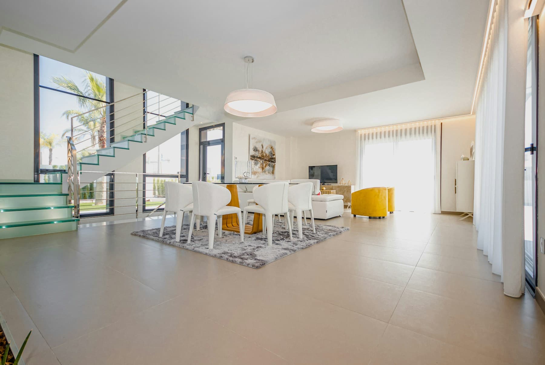 Bright modern Spanish villa with white dining furniture and glass staircase.