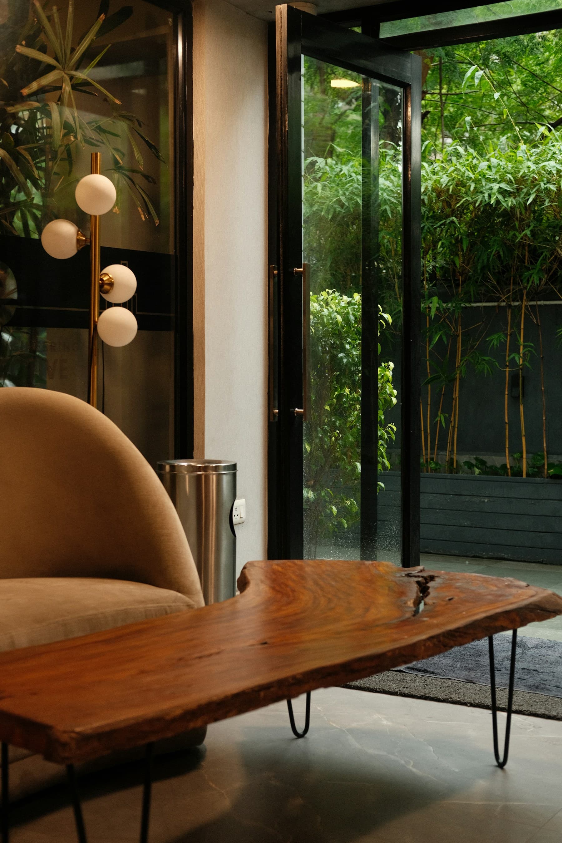 Live-edge timber coffee table and soft lounge chair beside a bamboo garden.