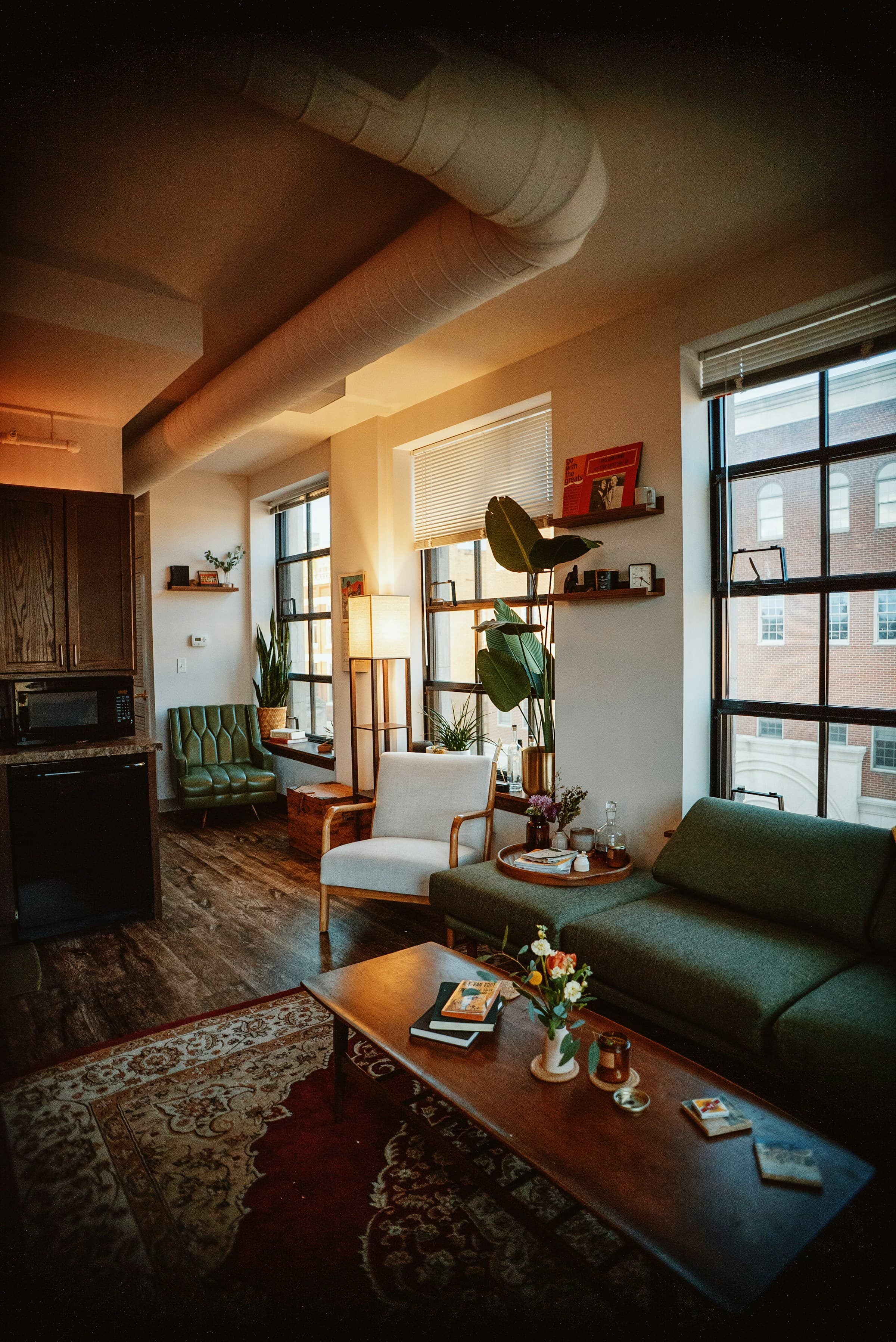 Warm urban loft with green seating, timber tables and tall factory windows.