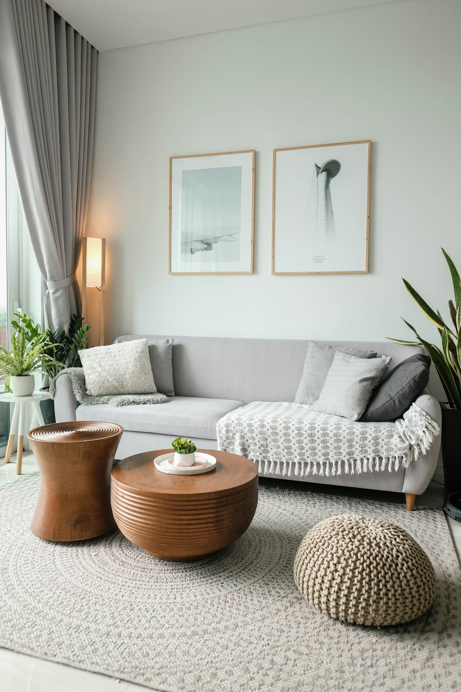Grey sofa and sculpted timber tables beside a full-height curtained window.